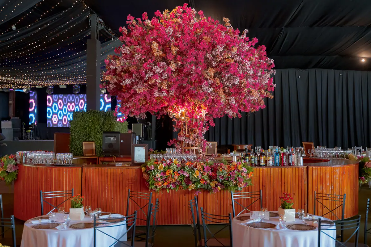 Salão montado com bar, mesas e arranjo suspenso de flores